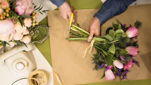 Free photo a male florist pruning the stem of flowers bouquet in the flower shop