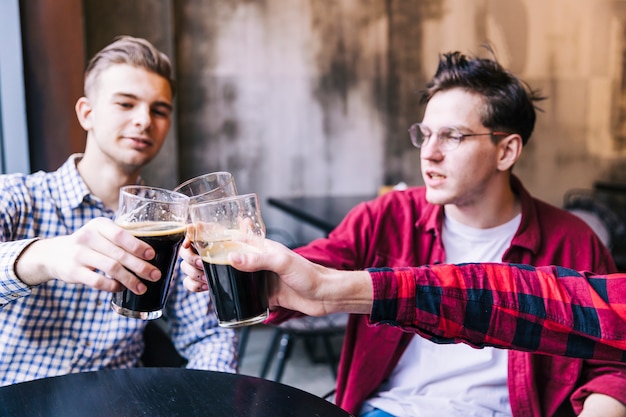 Male friends clinking the beer glasses over the table