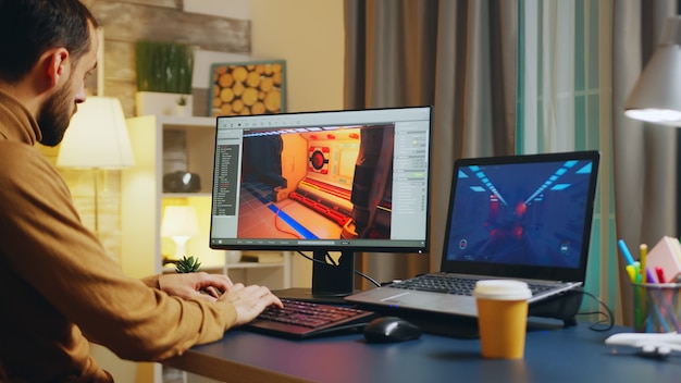 Male game developer typing on keyboard while developing a new level of the game.