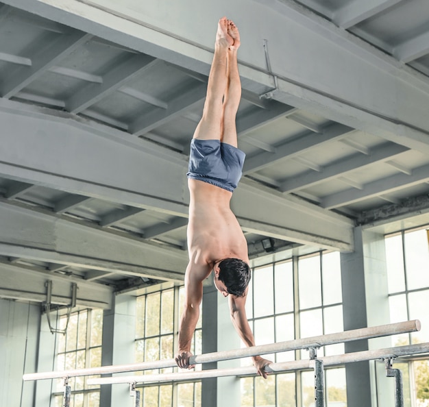 Free Photo male gymnast performing handstand on parallel bars