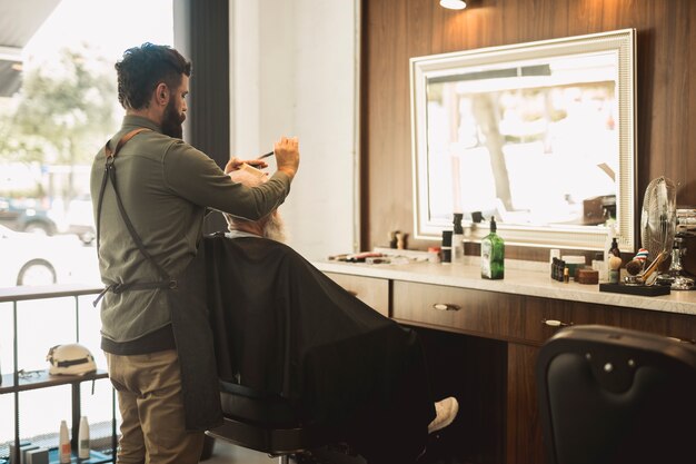 Male hairdresser combing hair of senior client