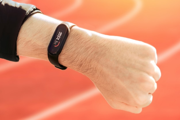 Free Photo a male hand clenched into a fist with fitness bracelet and training progress on it, running tracks on the background