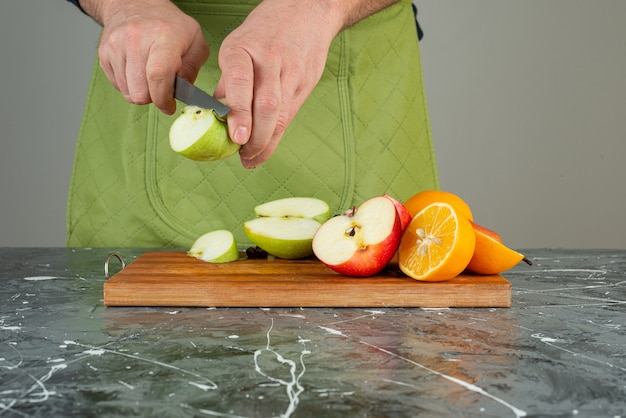 Free photo male hand cutting fresh apple on top of wooden board on table.