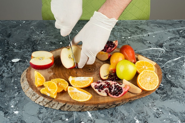 Male hand cutting fresh red apples on marble table.