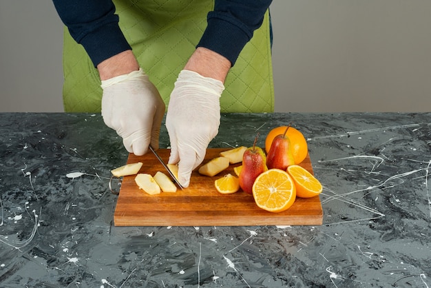 Male hand cutting fresh red apples on marble table.