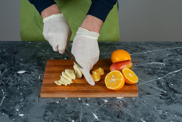 Male hand cutting green apple on marble table.