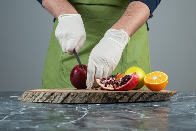 Free photo male hand cutting red apple on top of wooden board on table.