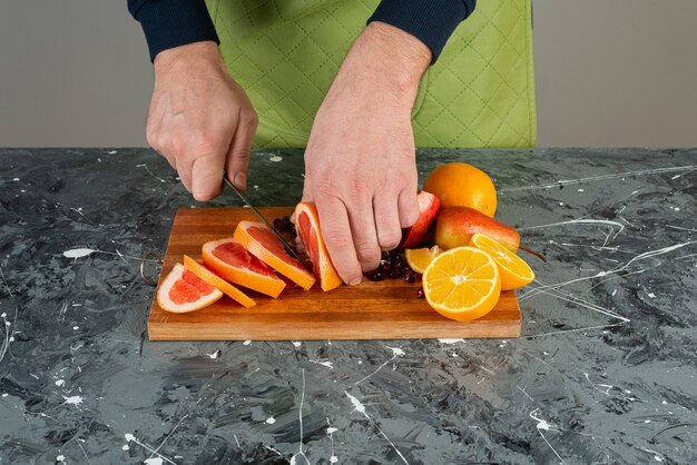 Male hand in gloves cutting juicy grapefruit on marble table.