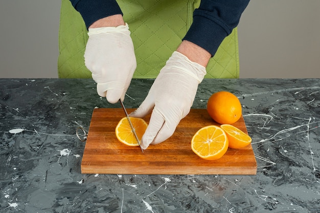 Free Photo male hand in gloves cutting juicy orange on marble table.