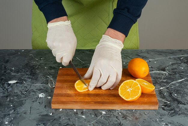 Male hand in gloves cutting juicy orange on marble table.