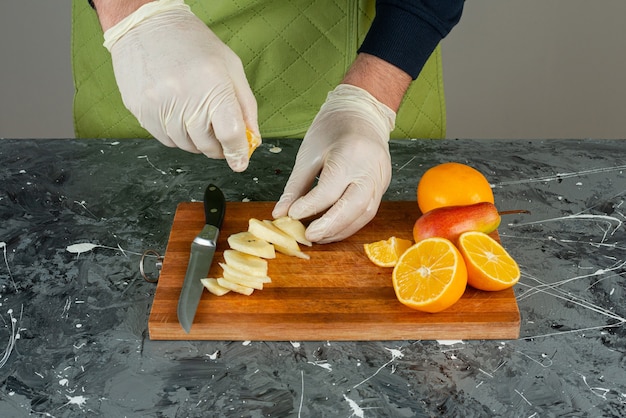 Male hand in gloves squeezing lemon juice into the apples on top of wooden board.