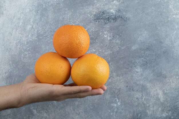 Male hand holding three oranges on marble table. 