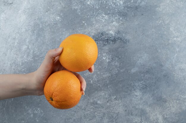 Male hand holding two oranges on marble table. 