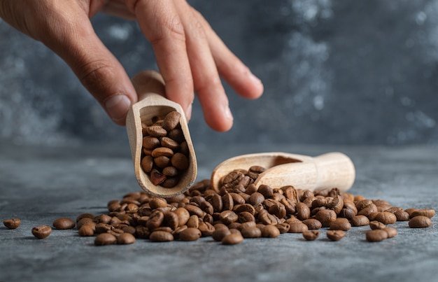 Free Photo male hand holding wooden spoon of aromatic coffee beans on marble background