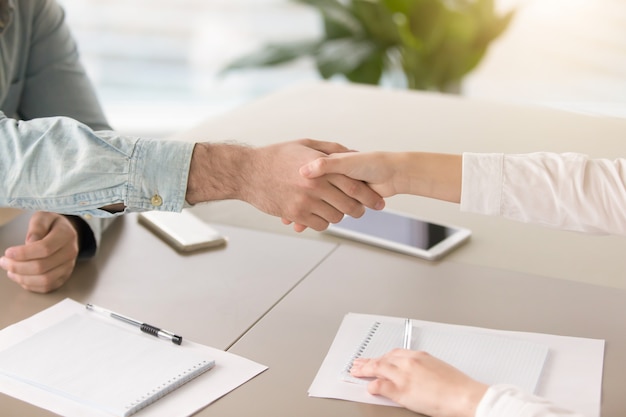 Male hand shaking hand of young female over office desk