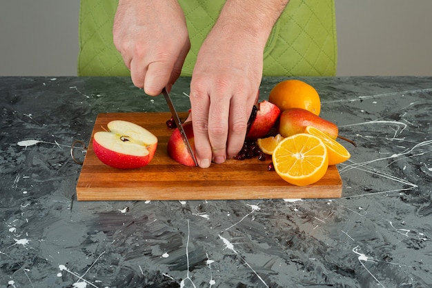 Male hand slicing red apple on top of wooden board on table.