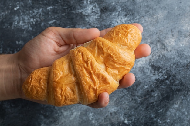 Male hands holding fresh croissant on marble background