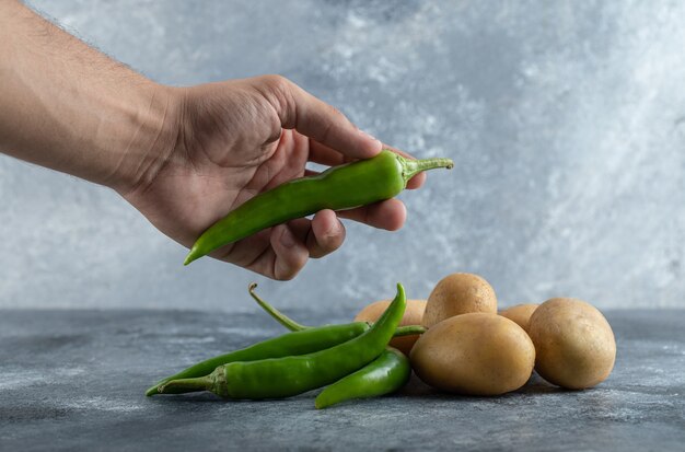 Male hands holding green chili peppers on marble background