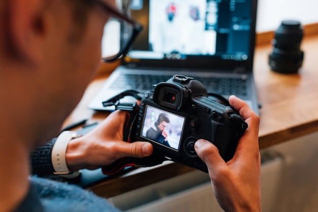 Free photo male hands holding professional camera, looks photos, sitting at cafe with laptop.