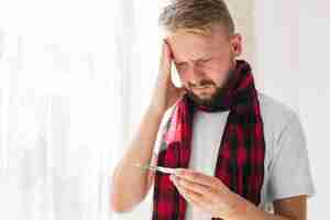 Free photo male having fever and looking at thermometer