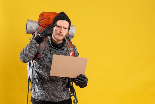 male hitchhiker with leather gloves and backpack holding blank cardboard thinking