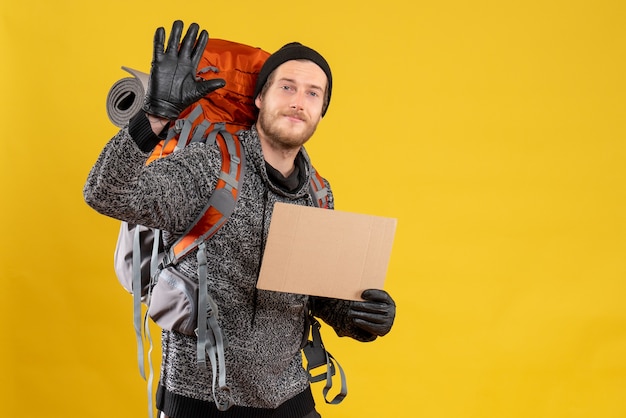 Free photo male hitchhiker with leather gloves and backpack holding blank cardboard waving hand