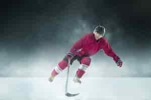 Free photo male hockey player with the stick on ice court and dark wall