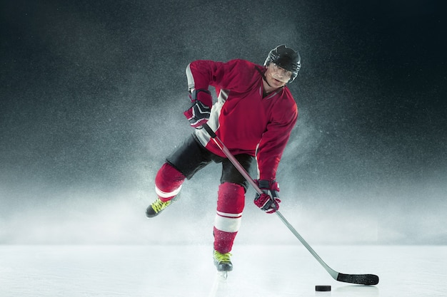 Male hockey player with the stick on ice court and dark wall