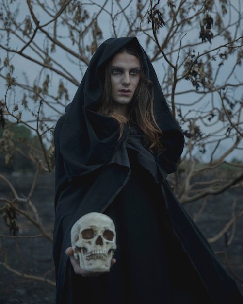 Free Photo male mage in black clothes looking away with skull in hand