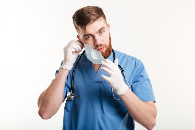 Male medical assistant with stethoscope taking his mask off