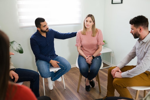 Free photo male member at an aa meeting comforting a caucasian woman during a group therapy session. sad pretty woman attending a support group