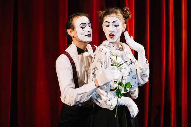 Free photo male mime artist giving white rose to female mime