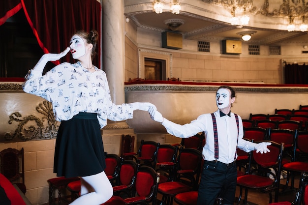 Free photo male mime artist holding shy female mime's hand in auditorium