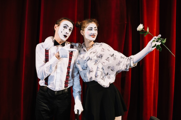 Free photo male mime artist pointing toward female mime holding white rose