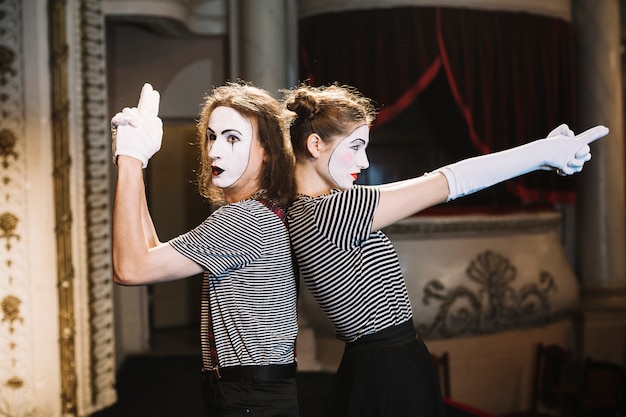 Male mime and female mime standing back to back making hand gun gesture