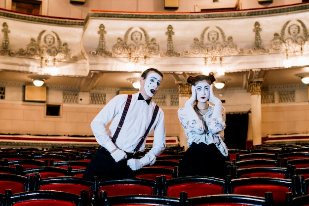 Male mime posing near the sad female mime sitting on chair