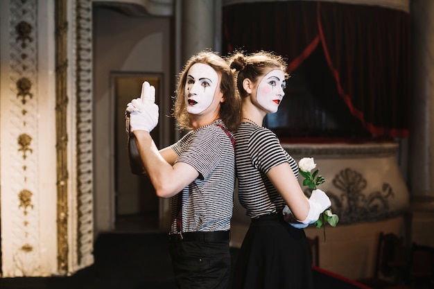 Male mime with hand gun gesture and female mime holding rose standing back to back