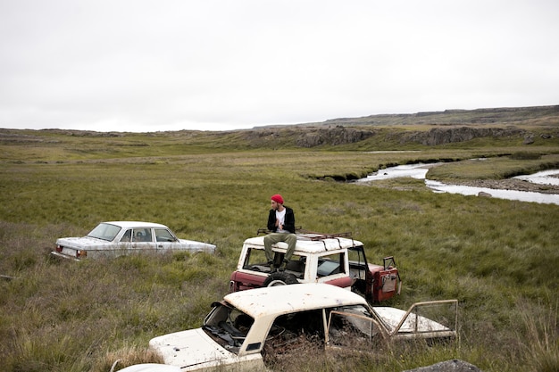 Free photo male model in cool outfit on top of car in junk yard