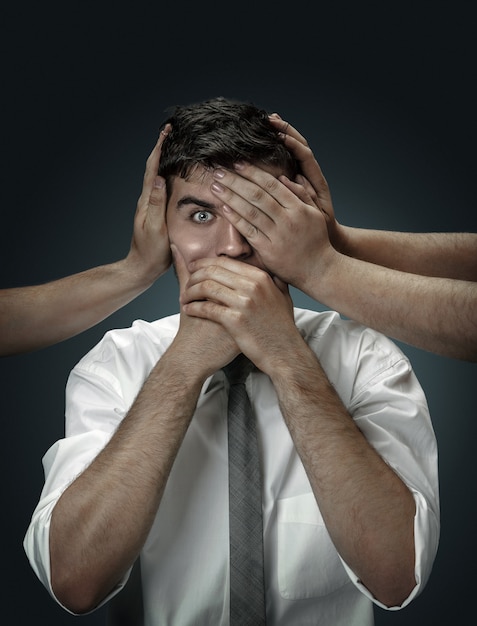 A male model surrounded by hands like his own thoughts on dark wall