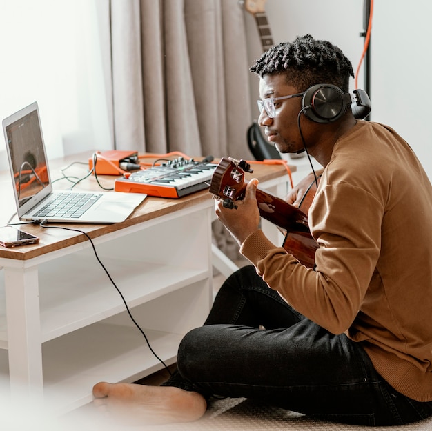 Free Photo male musician at home playing guitar and mixing with laptop