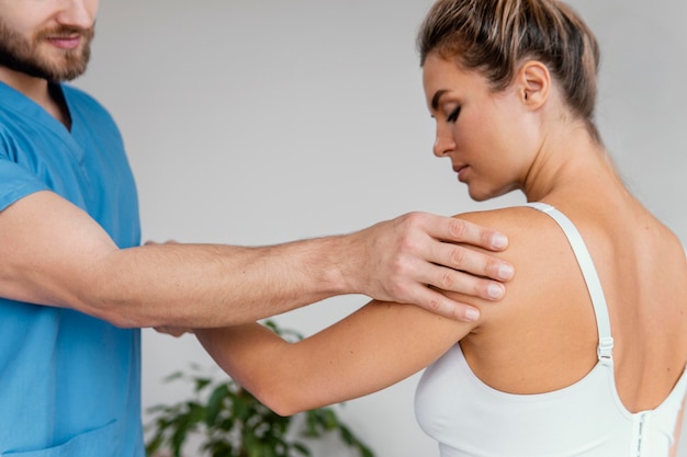 Male osteopathic therapist checking female patient's shoulder pain