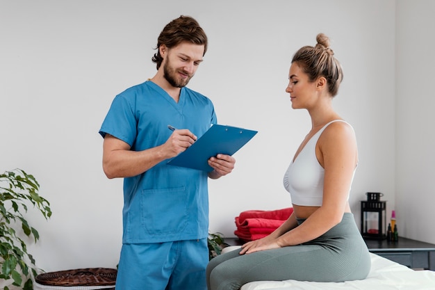 Free photo male osteopathic therapist with female patient signing clipboard at the clinic