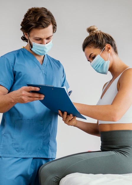 Male osteopathic therapist with medical mask and female patient in the office signing clipboard