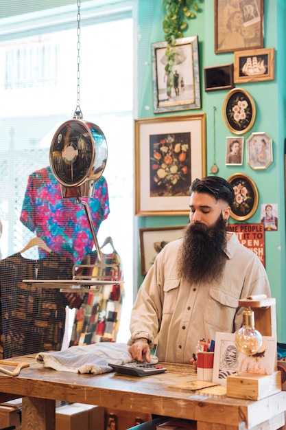 Free Photo male owner making calculation on calculator in his clothes store