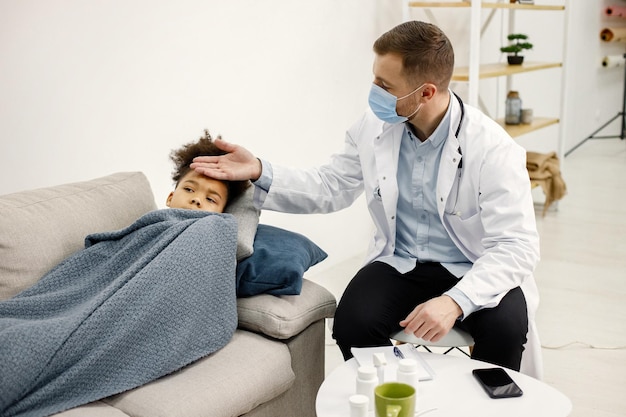 Male pediatrician holding hand on a forehead of sick little black girl