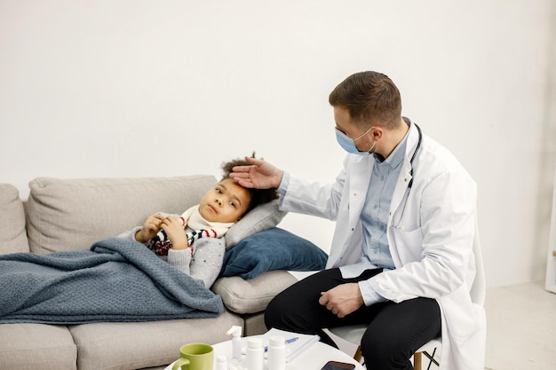 Male pediatrician holding hand on a forehead of sick little black girl