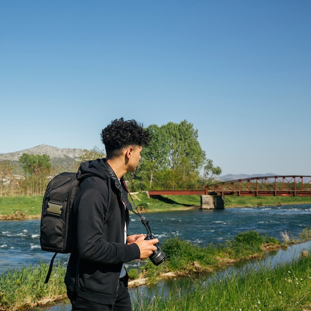 Free photo male photographer carrying backpack and camera hiking near beautiful river