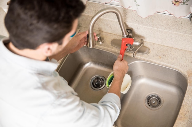 Free photo male plumber using a wrench to tighten a water faucet in a kitchen, seen up close