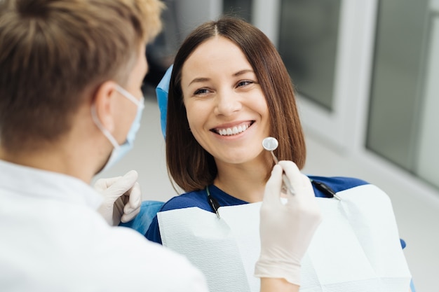 Male Professional Dentist With Gloves And Mask And Discuss What The Treatment Will Look Like Of The Patient's Teeth