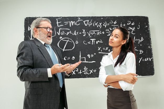 Male professor and young woman against chalkboard in classroom